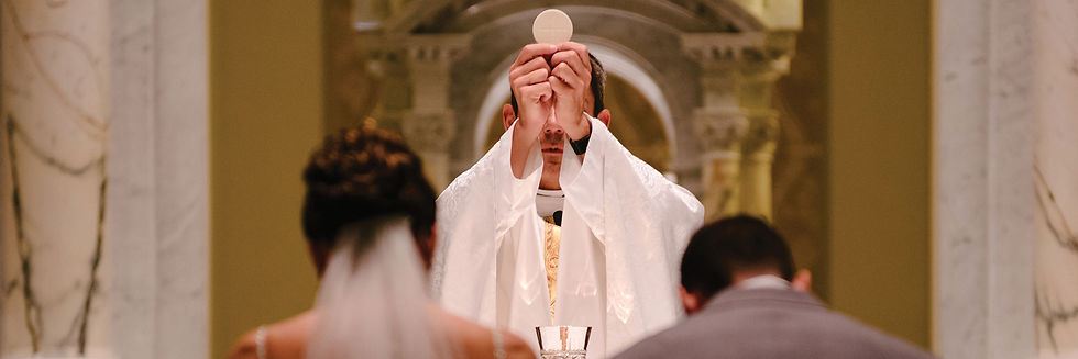 A priest holding up the host during consecration while a bride and groom kneel in front of the altar